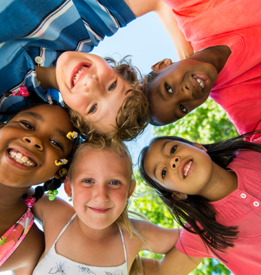 Group of five multi-racial children hugging and looking at the camera in a circle.