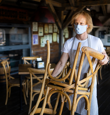 Masked restaurant owner putting chairs back out in dining area.