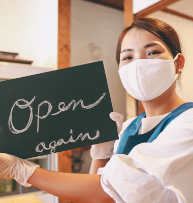 Young female restaurant owner wearing mask and holding up