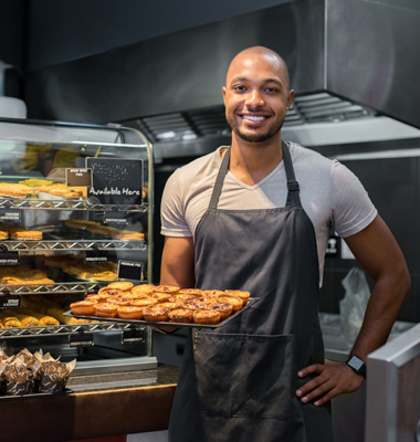 Smiling bakery owner holding tray of freshly-baked pastries.
