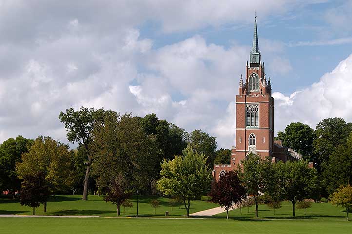 Beautiful brick church with tall steeple on a green lawn, surrounded by trees.