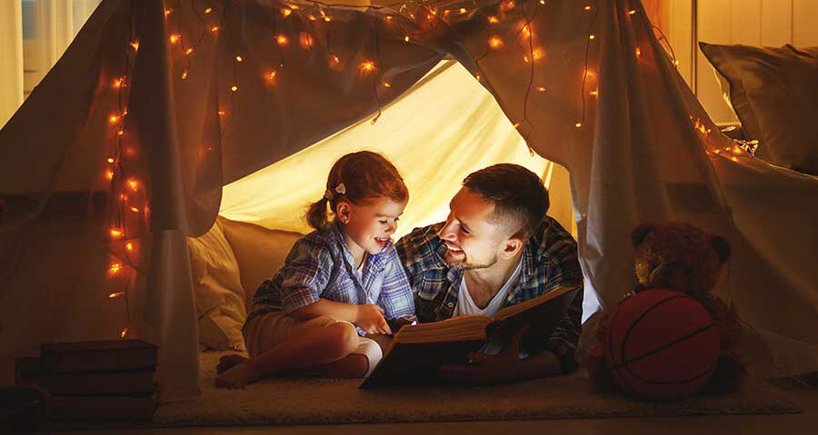 Father and daughter reading book in homemade tent.