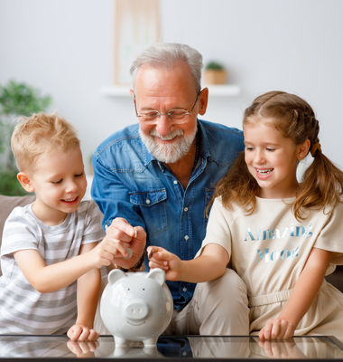 Grandfather and two grandchildren putting money into a piggy bank.