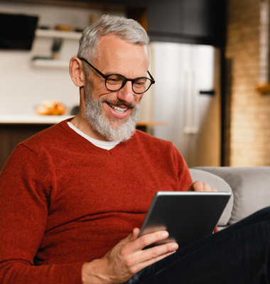 Mature gentleman sitting on couch looking at smart tablet.