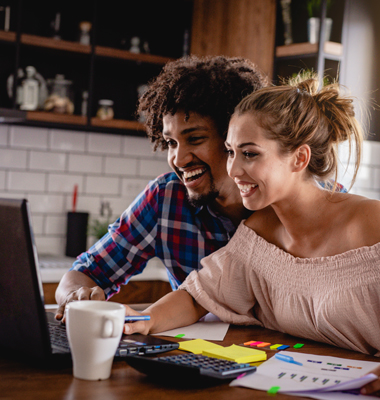 Happy young couple at kitchen table on laptop.