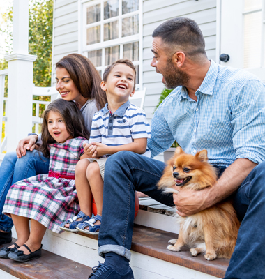 Happy family with dog sitting on front step of home.