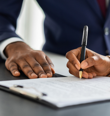 Hand shown signing a document, with banker in suit nearby.