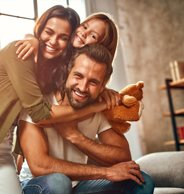 Mother, father and young daughter hugging in family living room.