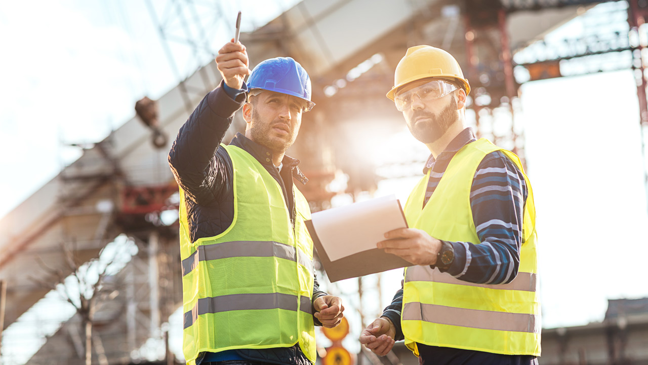 Two men in construction gear surveying worksite.