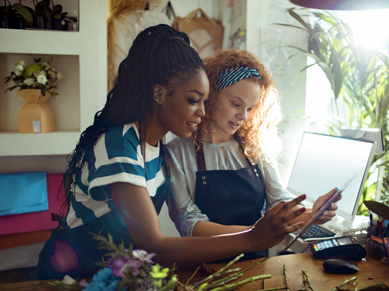 Young female business owners in floral shop setting up payment service on a smart tablet.