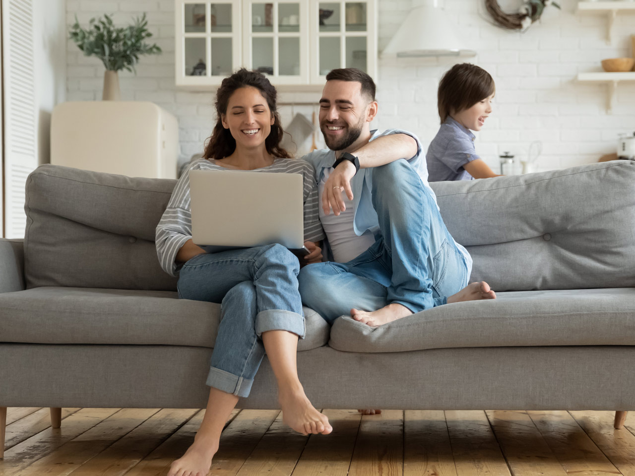 Young mother and father on laptop in living room while children play.