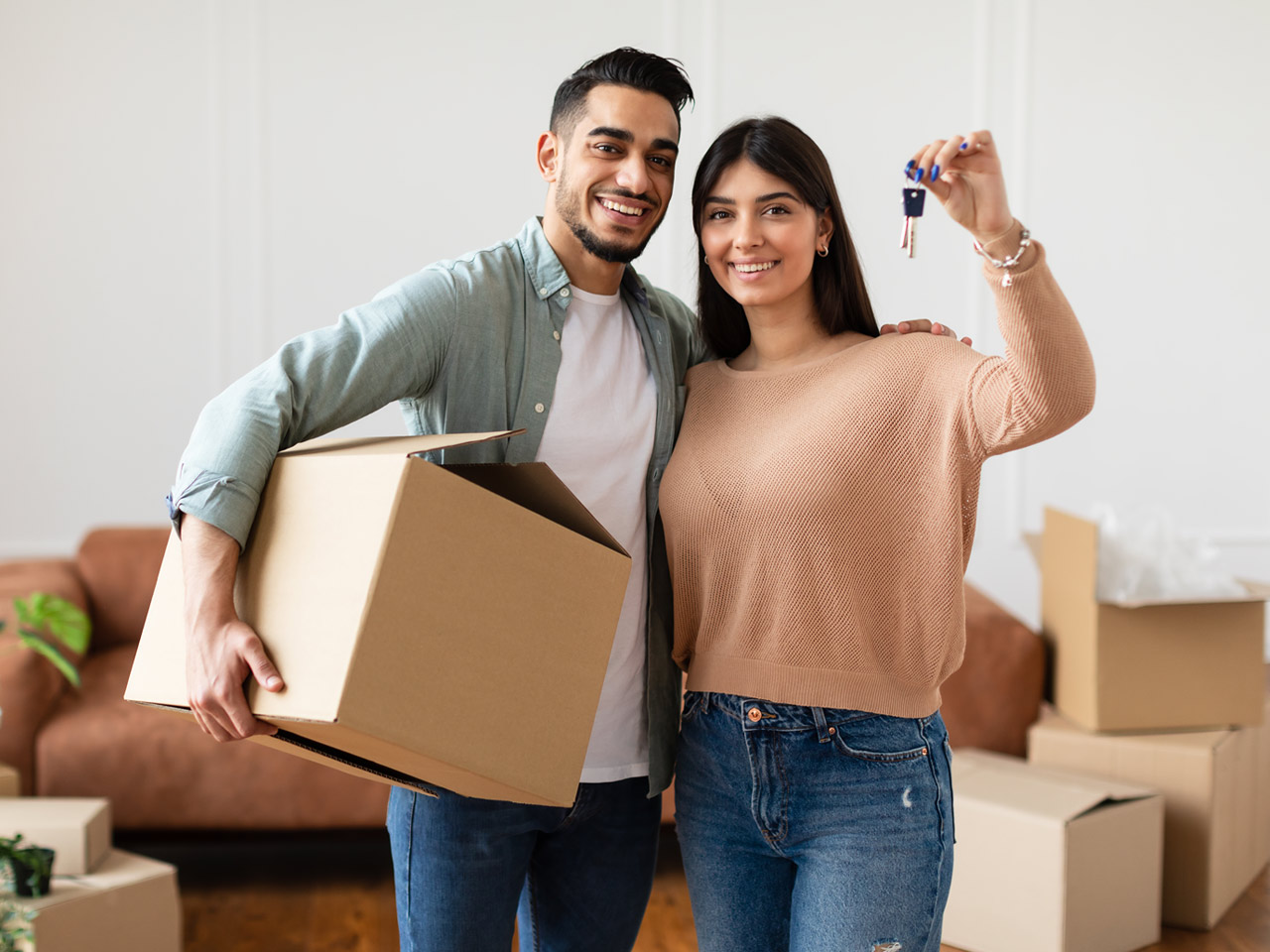 Young couple holding up keys inside new home.