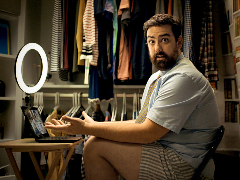 Man sitting in cramped closet office attending online meeting.