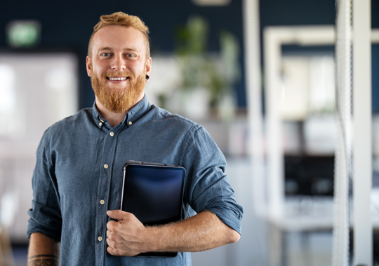 Happy young man holding smart tablet and standing in office.