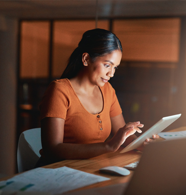 Woman sitting at desk reviewing info on smart tablet.