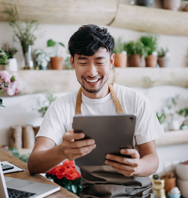 Young male botanical shop owner reviewing business account on smart tablet.