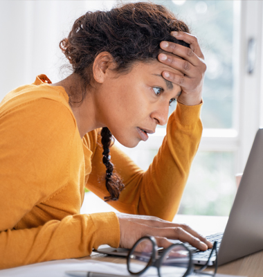 Distressed woman sitting at table and looking at laptop screen