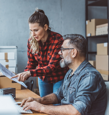 Female business owner and mature male account manager reviewing past due invoices on computer screen.