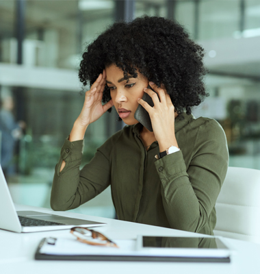 Concerned young woman on smartphone looking at laptop screen.