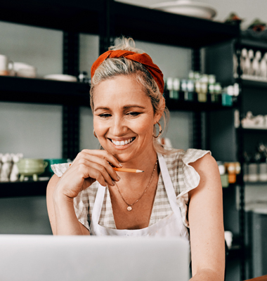 Woman working in her pottery shop, reviewing customer info on laptop.
