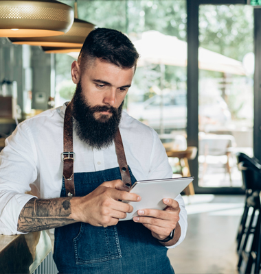 Young male coffee shop manager reviewing transactions on a tablet.
