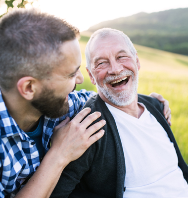 Grown son with elderly father laughing together in the park.