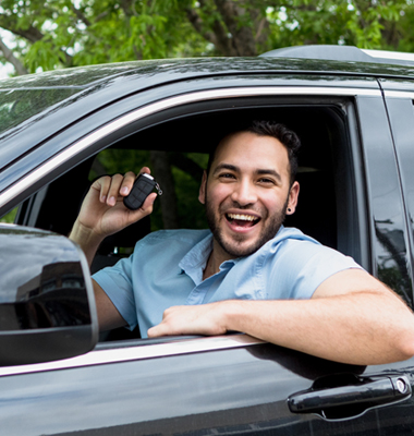 Smiling young man sitting in his new car and holding up keys