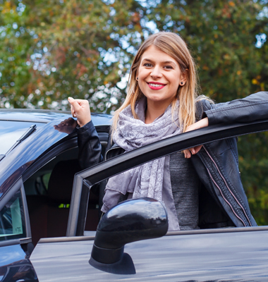 Young woman leaning on door of her new car.