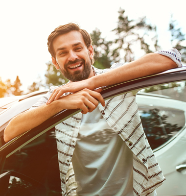 Young bearded man smiling and leaning on car door.
