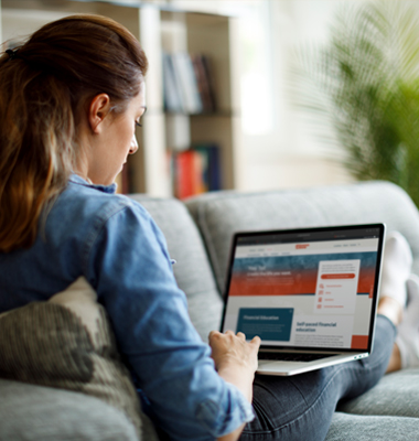 Woman reclining on couch looking at 1st Source website on laptop.