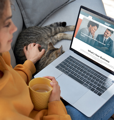 Young woman sitting on couch with cat and viewing 1st Source business website on laptop.