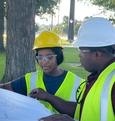David Jackson and his daughter Makenna in hardhats and safety vests reviewing a demolition plan.