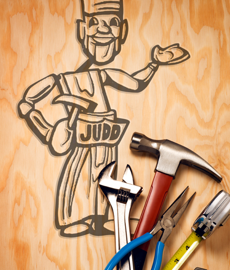 Tools laying on a piece of plywood with the Judd Lumber carpenter cartoon character engraved.