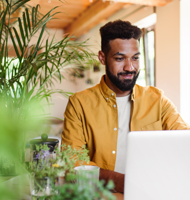 Young man using laptop in brightly lit dining area.