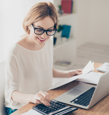 Young woman at home office using calculator and laptop.