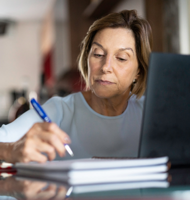 Accountant using laptop and pen and paper to review loan and debt information.