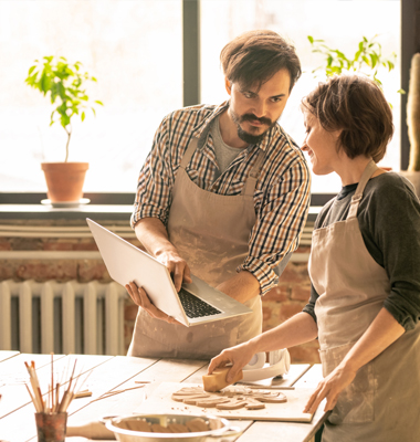 Male and female woodcraft shop owners reviewing financial info on laptop.