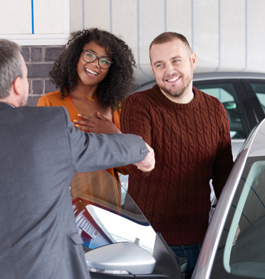 Young couple buying a car, shaking hands with the dealer.