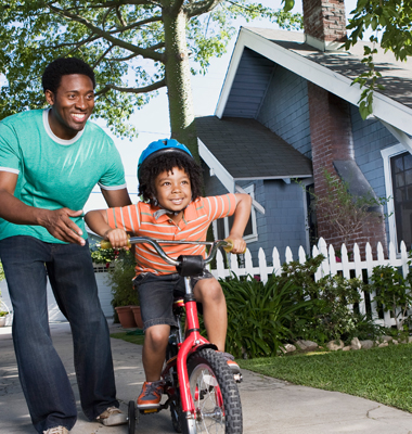 Father teaching child how to rid bicycle in front of their suburban home.