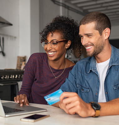 Young couple calculating credit card payments on laptop at kitchen table.