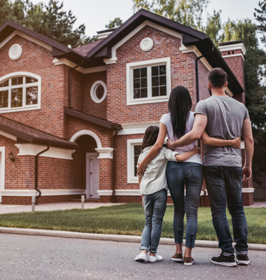Mother, father and daughter standing in front of brick home.