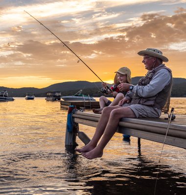 Grandfather teaching grandson how to fish off of pier.