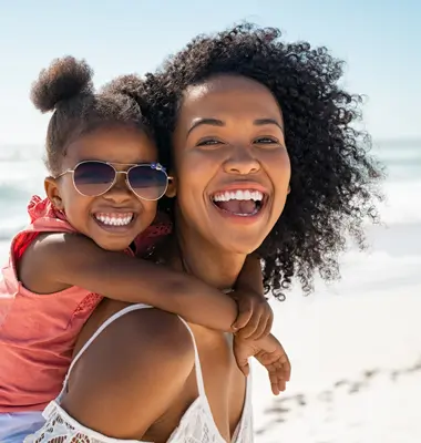 Young mother with daughter riding piggyback, laughing on the beach.