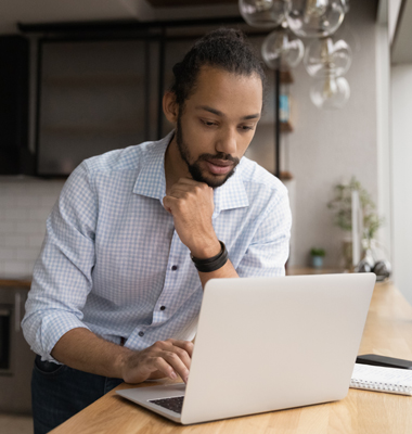 Man sitting in kitchen working at laptop.