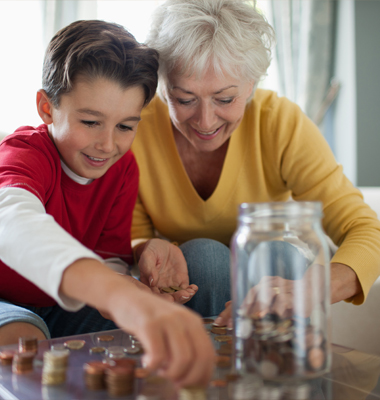 Grandmother counting loose change with grandson on living room table.
