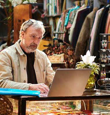 Owner of vintage shop handling accounting on laptop at store counter.