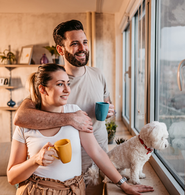 Young couple with their small dog looking out kitchen window.