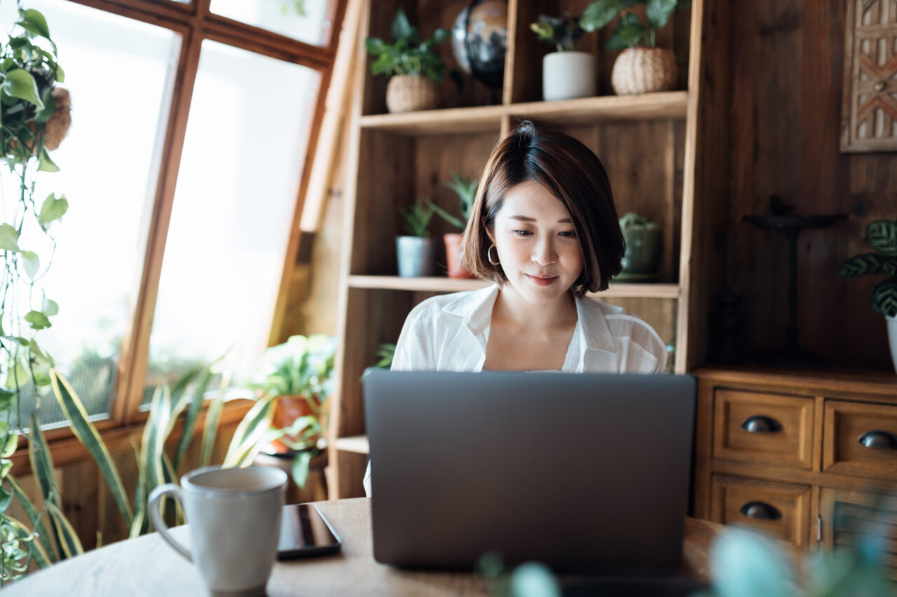 Young Asian woman managing online banking on laptop, taking care of her money and finances while relaxing at home. Banking with technology