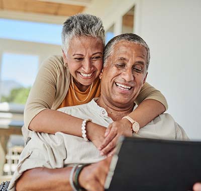 A mature couple relaxing on a couch, engaged with a laptop in front of them.
