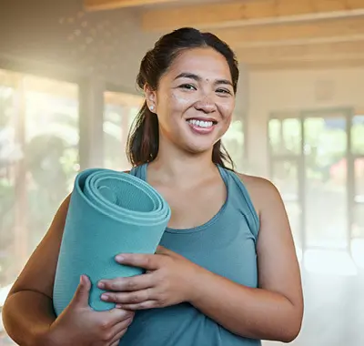 a smiling woman holding a yoga mat